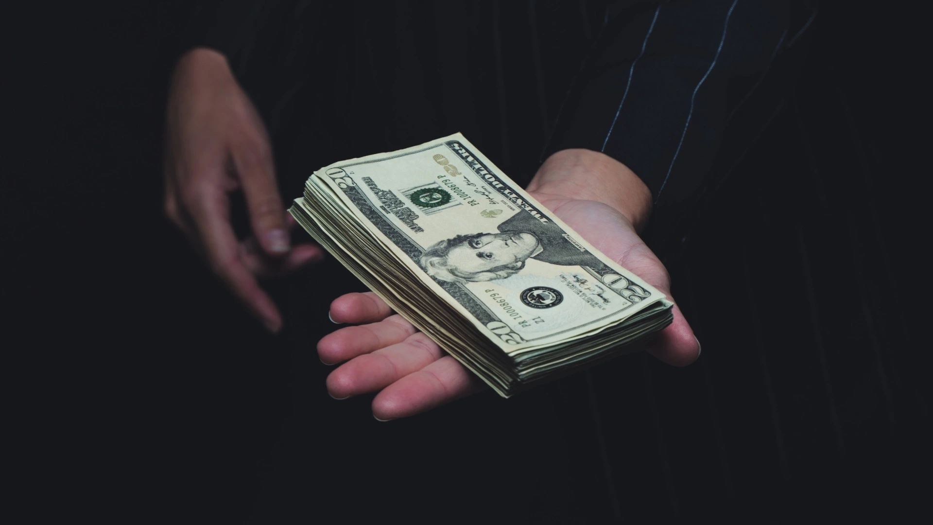 Close-up of an investor's hand handing over dollar bills, representing secured capital and increased valuation.