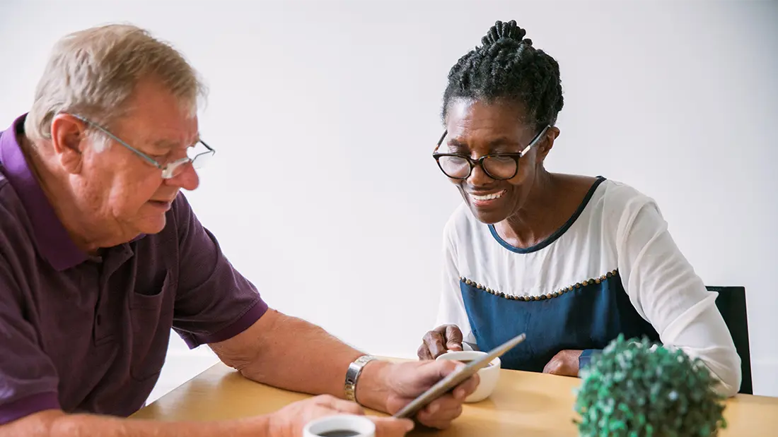 Elderly couple enjoying a tablet at a table.