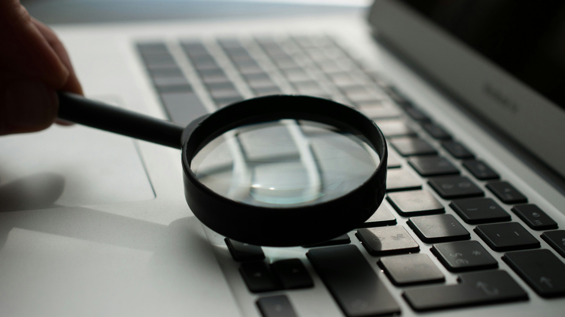 Close-up of a magnifying glass positioned above a laptop keyboard as a UX Audit