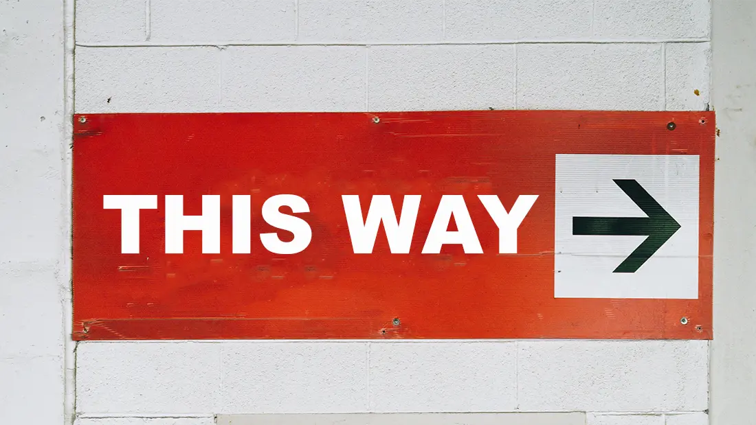 A weathered red sign with white lettering reading "THIS WAY" and a black arrow pointing right.