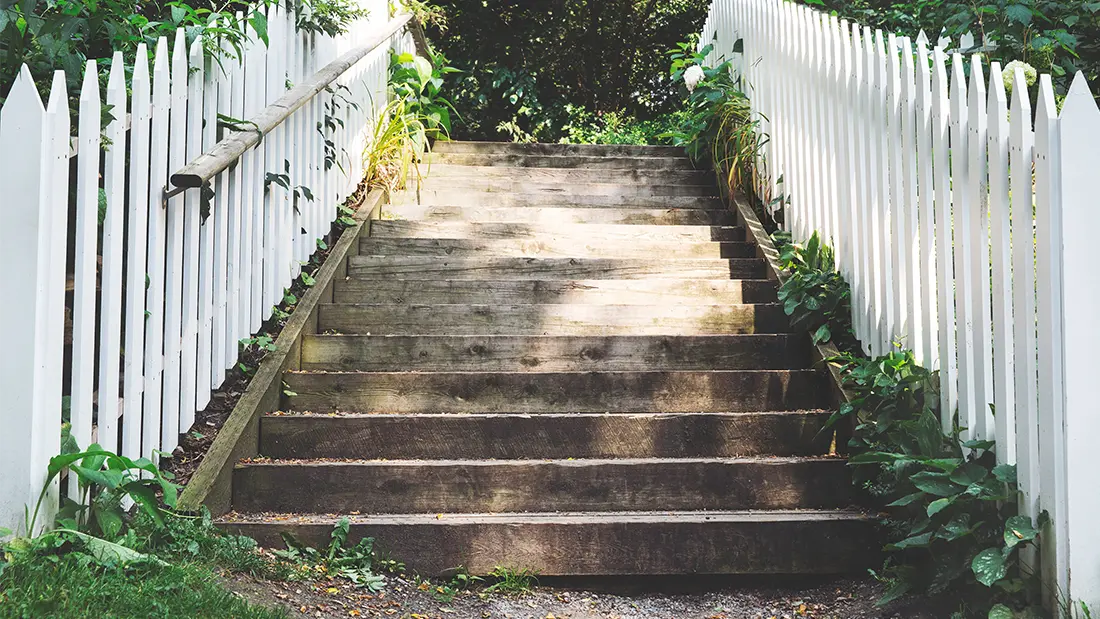 Looking up a set of stairs with picket fences on either side. The green plants and flowers around and at the top of the steps makes it look like we are going nowhere but up in the UX steps!